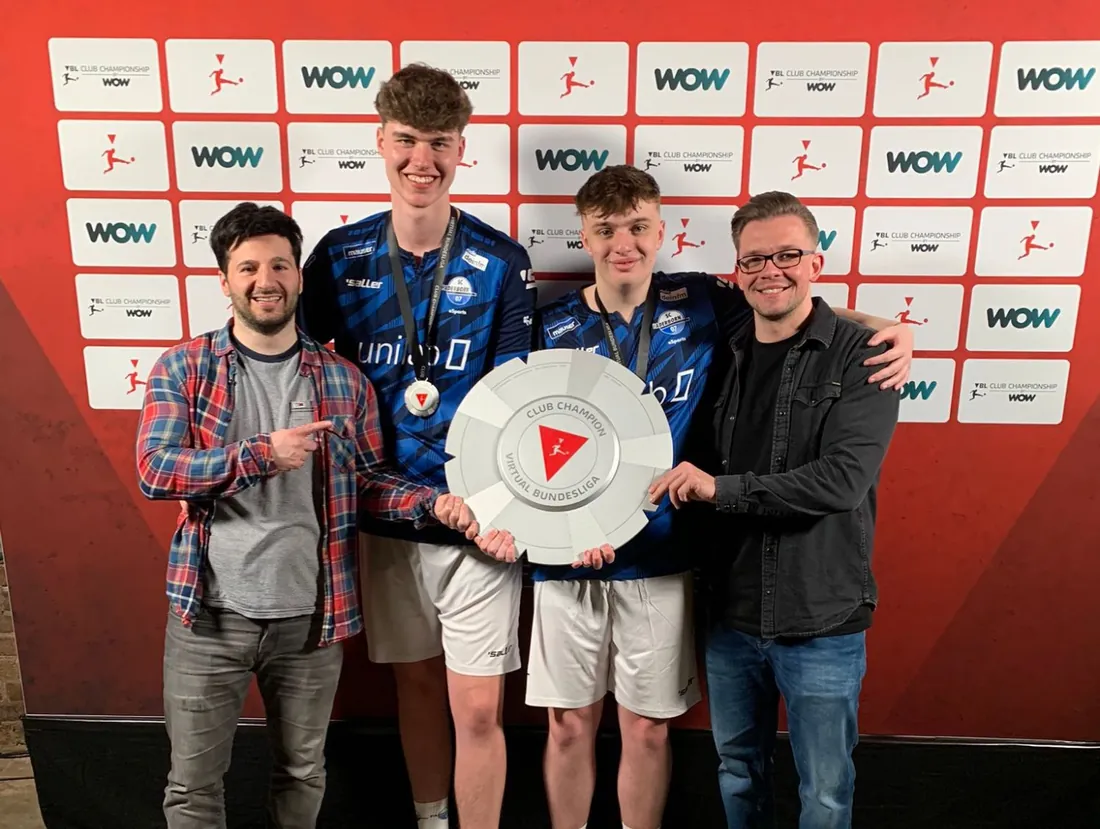 Erhan Kayman und Marvin Hintz mit ihrem Team bei der Siegerehrung der Virtual Bundesliga – die vier halten gemeinsam die Club-Champion-Trophäe
